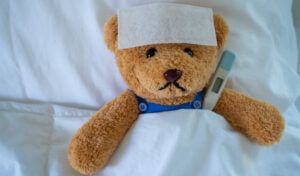Brown teddy bear with fever-reducing sheet and body temperature monitor. Used to show down with the sickness